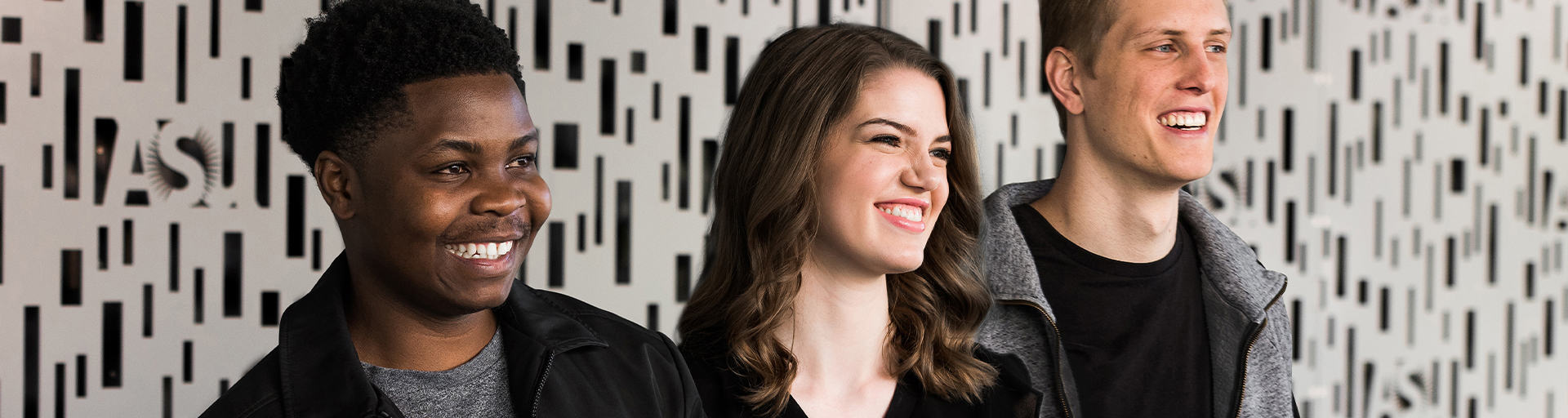 Three students smiling in front of a gray wall