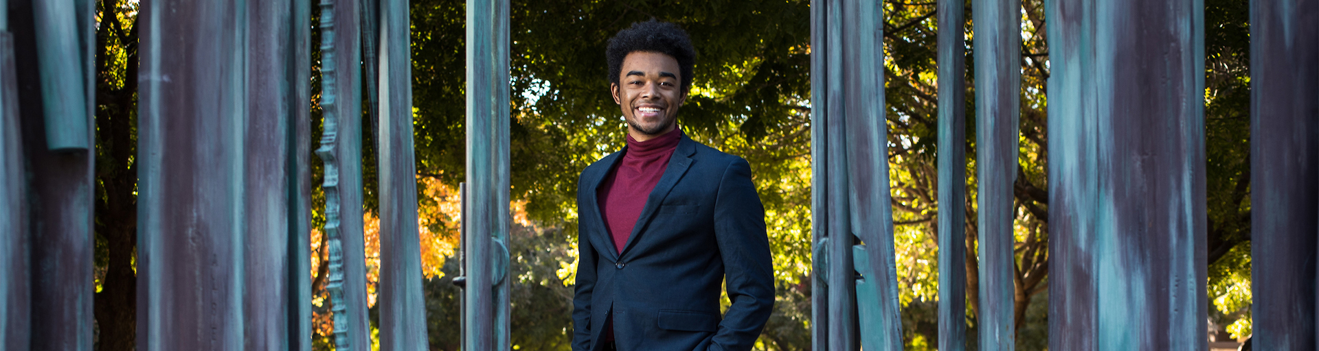 Student dressed in business attire in front of some trees on campus